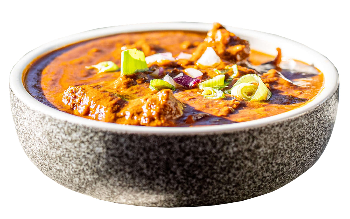 White bowl of orange curry with green onion garnish